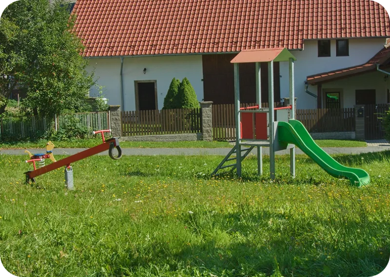 Dětské hřiště s houpačkou a skluzavkou na trávníku před statkem